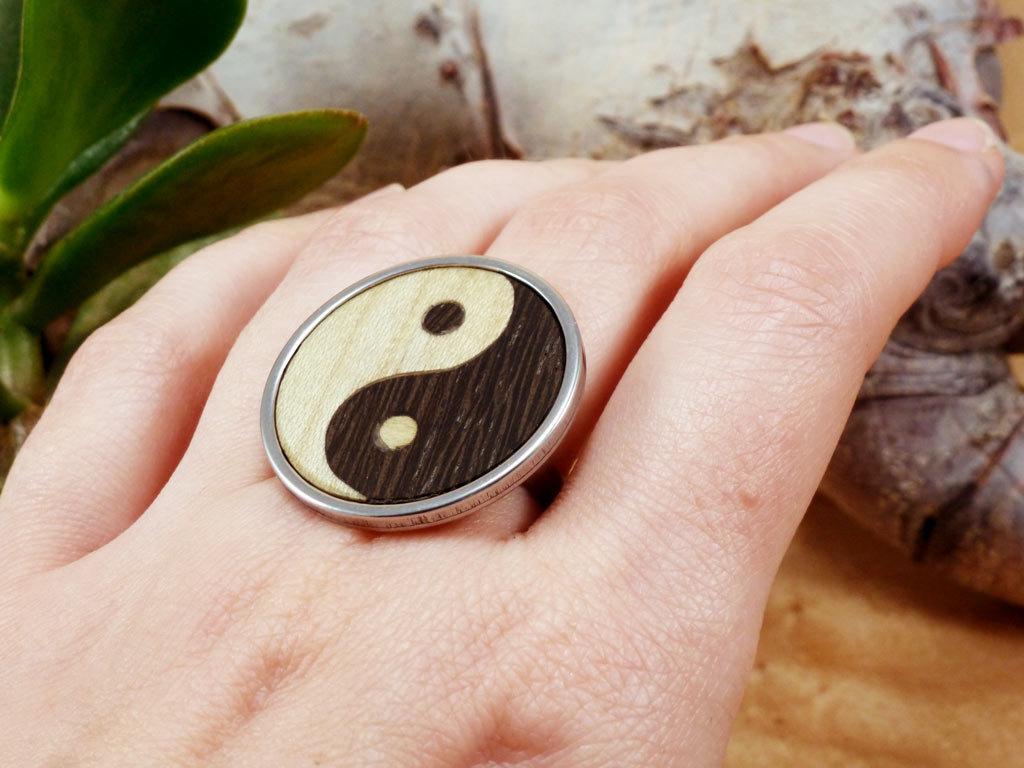 Anillo de acero hecho a mano con el símbolo del Yin Yang, elaborado con madera natural de wenge y sicomoro. Diseño único que fusiona tradición y artesanía moderna, ideal para quienes valoran la simbología y la sostenibilidad.
