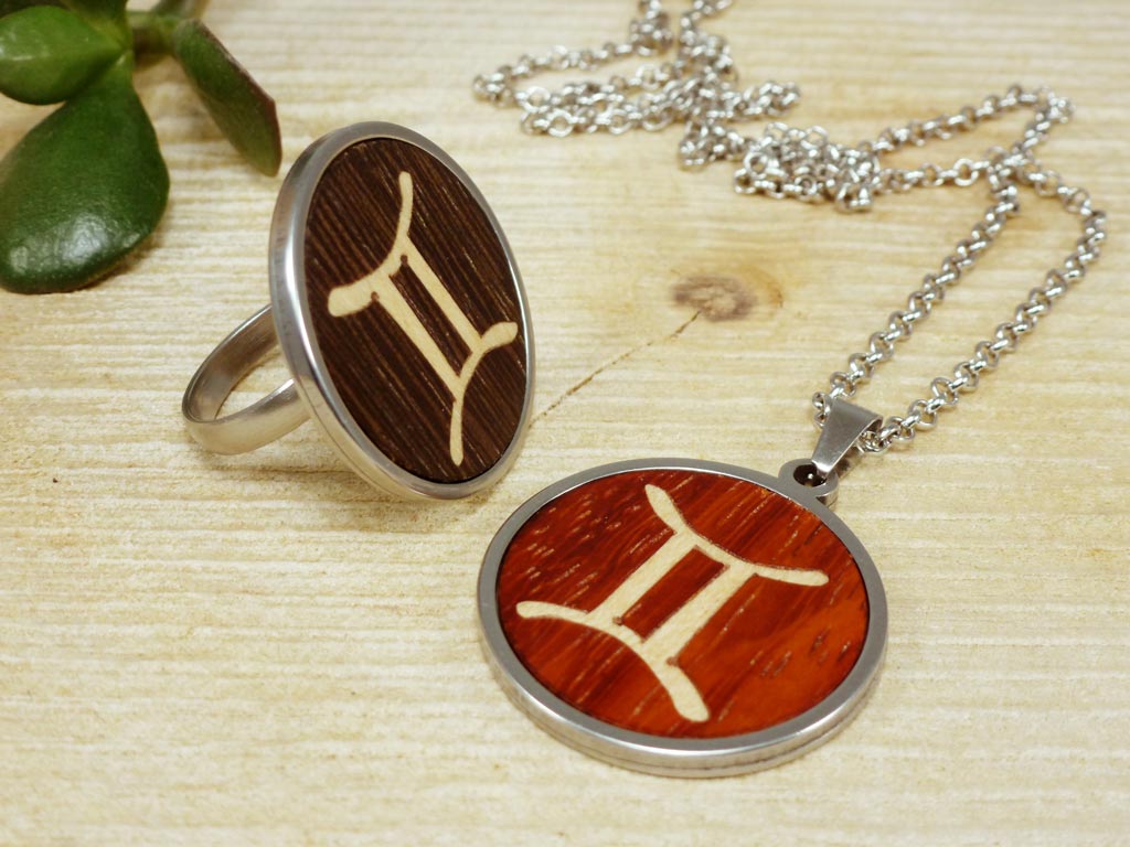 Conjunto de joyería de madera y acero con símbolo de Géminis, mostrando un colgante y un anillo artesanalmente tallados con el signo zodiacal. Accesorios ideales para amantes de la astrología y el diseño ecológico.