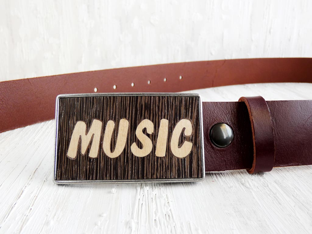 Hebilla de cinturón hecha a mano con la palabra 'Music' en marquetería, utilizando técnicas artesanales para incrustar madera en un diseño distintivo. Este accesorio no solo es funcional sino también una expresión de amor por la música, ideal para entusiastas y músicos que desean llevar un toque de su pasión en su vestimenta diaria.