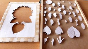 Foto de piezas detalladas de un girasol en marquetería, incluyendo pétalos y tallos cuidadosamente serrados, dispuestas sobre una mesa y listas para ser ensambladas en una obra de arte de marquetería.