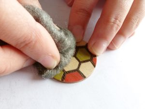 Puliendo cuidadosamente el barniz sobre un colgante de madera, aplicando los toques finales para lograr un acabado brillante y duradero. El detalle del trabajo manual resalta la calidad y la dedicación en la creación de joyería de madera.