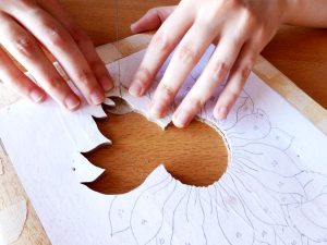 Serrando cuidadosamente los pétalos de un girasol de una pieza de marquetería. Cada movimiento meticuloso destaca la precisión y el arte en la creación de detalles florales en madera.