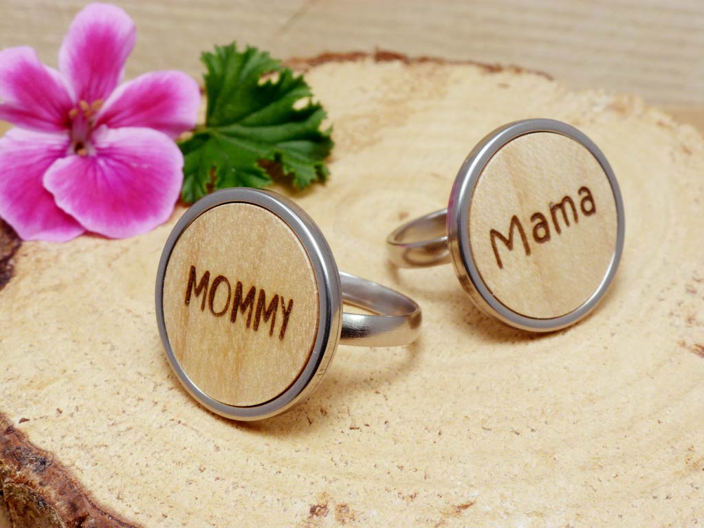 Dos anillos ajustables de madera de sicomoro y acero personalizados con el grabado de las palabras 'Mama' y 'Mommy'.