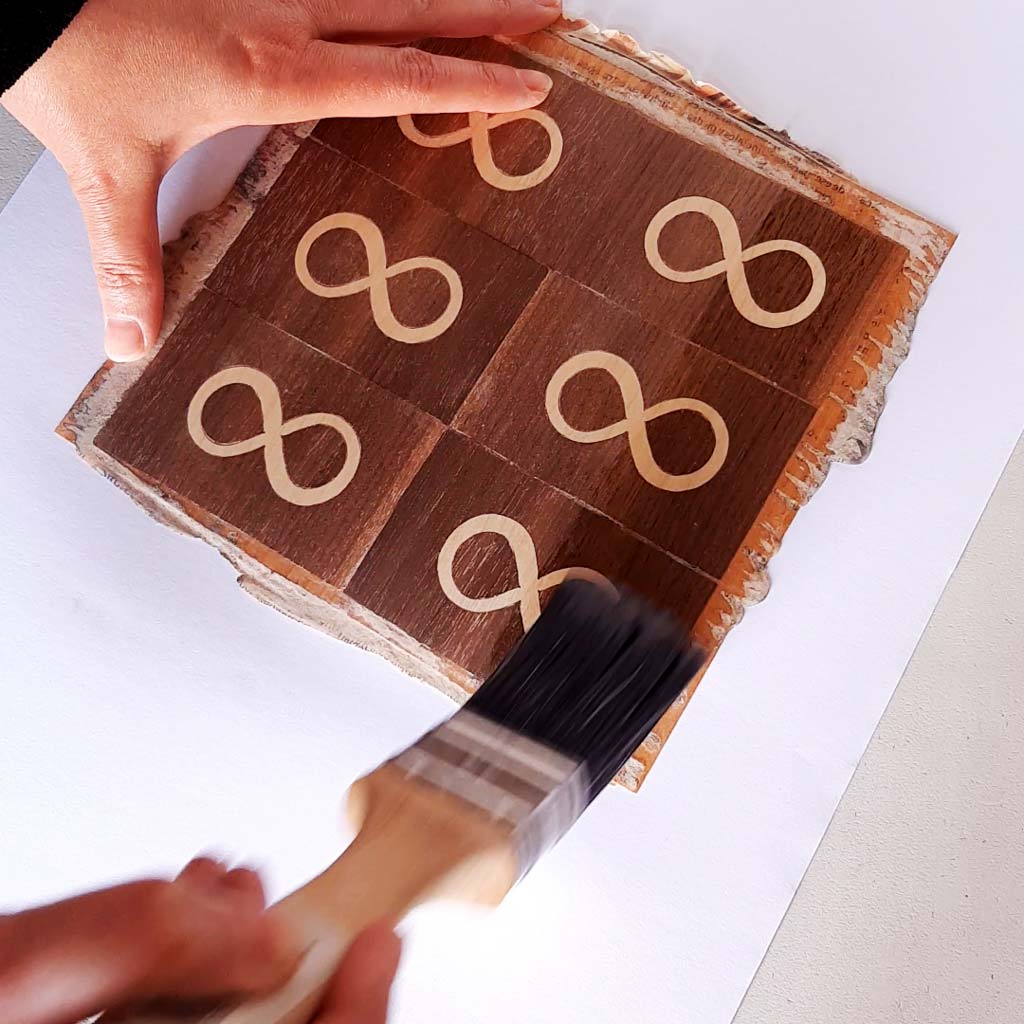 Momento en que se aplica barniz a una obra de marquetería para proteger y resaltar los detalles del intrincado diseño de madera. Se utiliza un pincel fino para asegurar una cobertura uniforme y realzar el acabado natural de la madera.