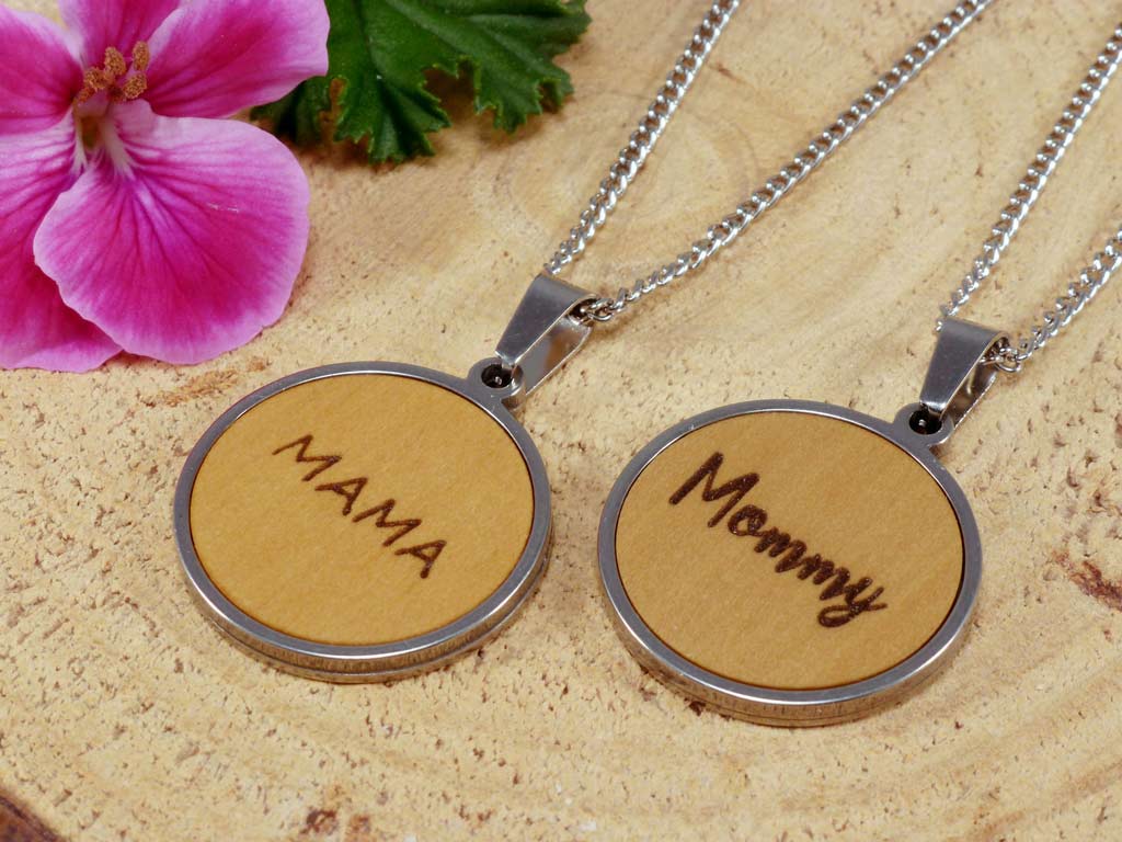 Dos colgantes redondos de madera de boj y acero personalizados con el grabado de las palabras 'Mama' y 'Mommy'.