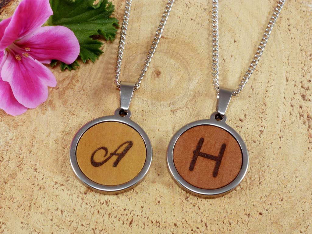 Dos colgantes pequeños de madera y acero personalizados con el grabado de una inicial, joyería personalizada artesanal.