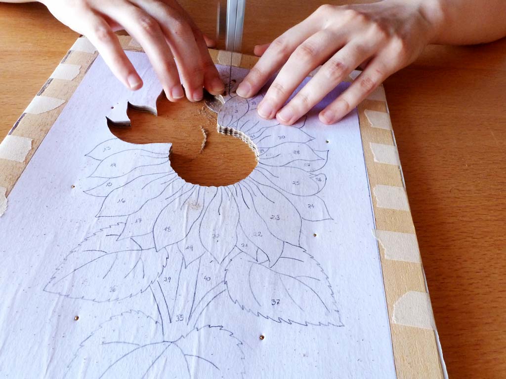 Serrando cuidadosamente la figura de un girasol en marquetería. Se utiliza una sierra de ballesta para cortar con precisión los detalles del diseño floral en madera, mostrando la habilidad y concentración necesarias en este arte.