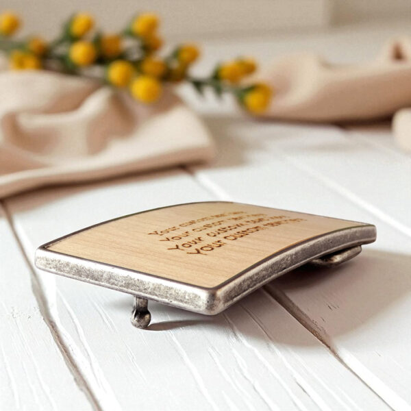 Unique personalized belt buckle with engraved custom message on wood.